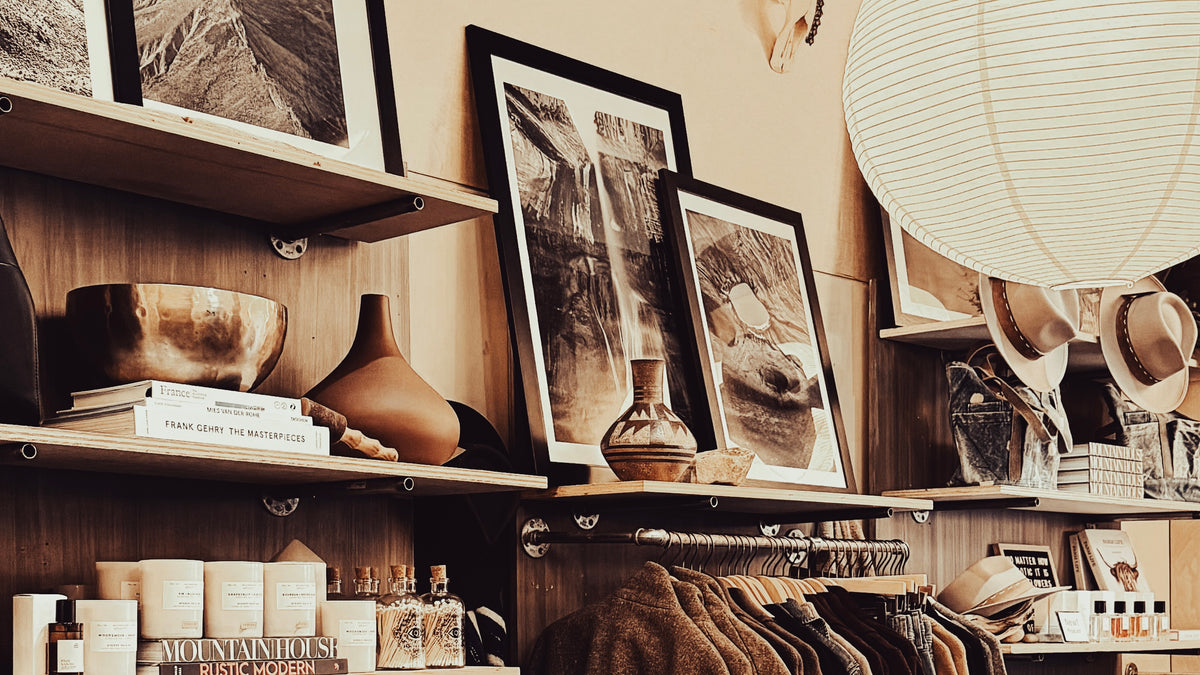 Shelves with framed artwork, decorative items, and clothing in a store setting.