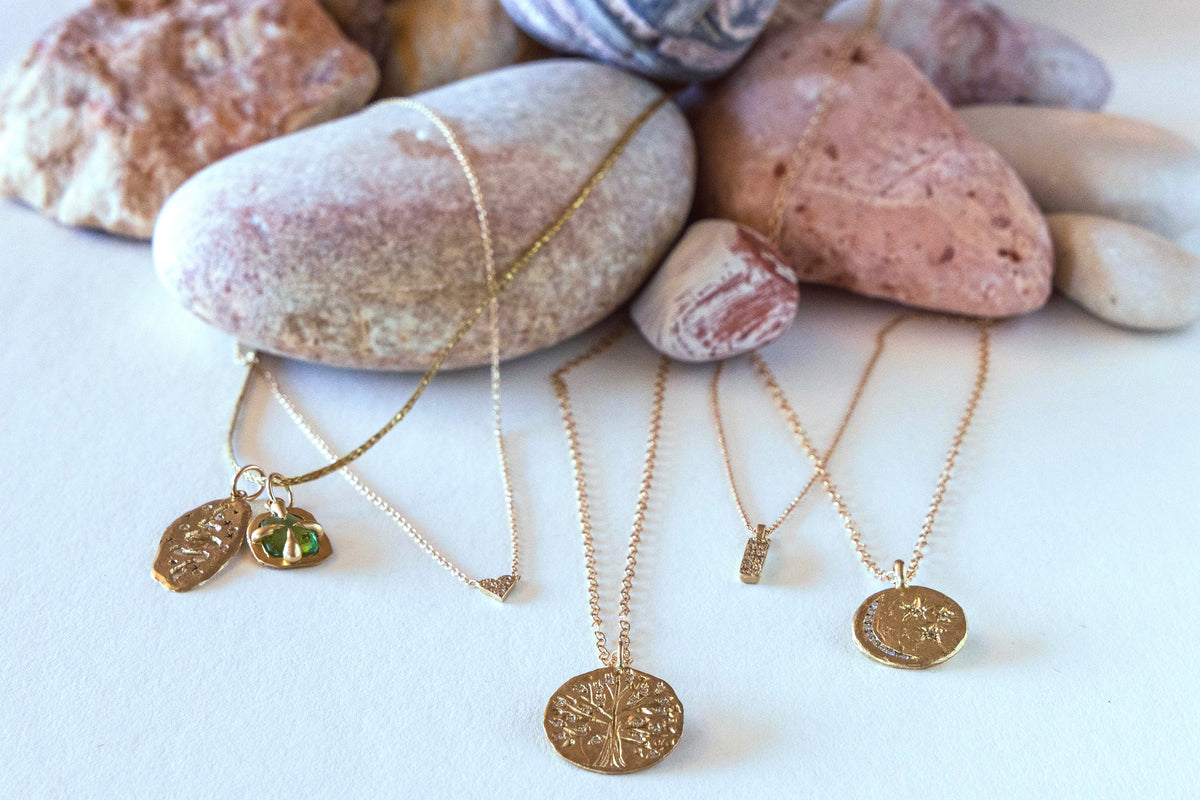 Gold necklaces with various pendants on a white surface with rocks in the background